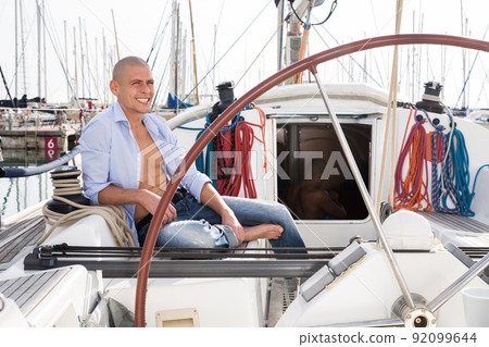 caucasian man topless with a bottle of beer in his hand sits on the deck of a yacht in seaport caucasian man topless with a bottle of beer in his hand sits on the deck of a yacht in seaport 92099644