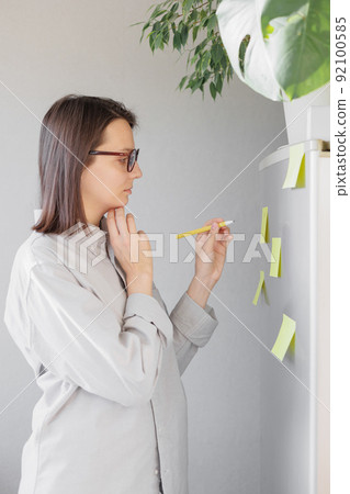 a woman makes notes on colored stickers on the refrigerator. a reminder or a note for her husband and children 92100585