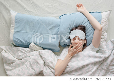 woman lies in bed and yawns or sleeps with a sleeping mask on her face. a European woman with sleep problems and insomnia 92100634