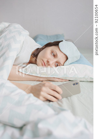 woman lies in bed and yawns or sleeps with a sleeping mask on her face. a European woman with sleep problems and insomnia woman lies in bed and yawns or sleeps with a sleeping mask on her face. a European woman with sleep problems and insomnia 92100654