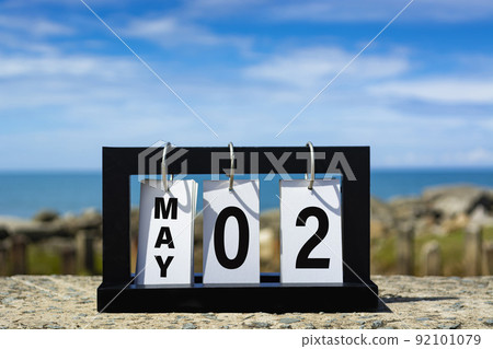 May 02 calendar date text on wooden frame with blurred background of ocean. 92101079