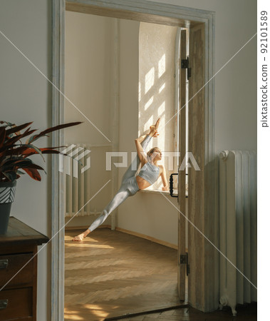 Fitness, yoga, stretching and healthy lifestyle concept - young woman doing exercises near window at home 92101589