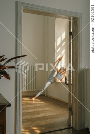 Fitness, yoga, stretching and healthy lifestyle concept - young woman doing exercises near window at home 92101591
