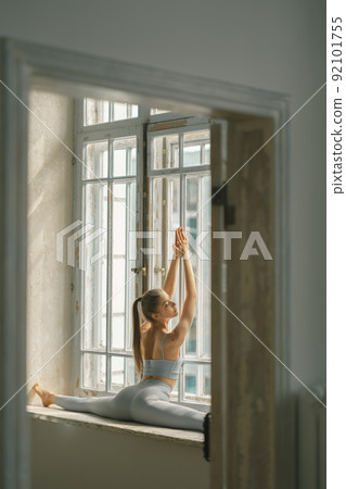Fitness, yoga, stretching and healthy lifestyle concept - young woman doing exercises near window at home 92101755