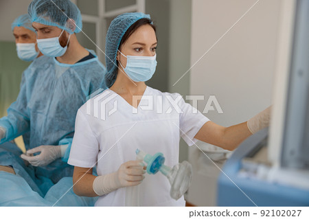 Nurse holding breathing mask in operating room before operation with colleagues on background 92102027