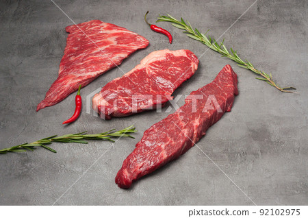 a mix of marbled beef steaks garnished with rosemary and chili pepper. Horizontal photo a mix of marbled beef steaks garnished with rosemary and chili pepper. Horizontal photo 92102975