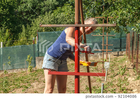 Young woman paints red primer metal structure 92104086