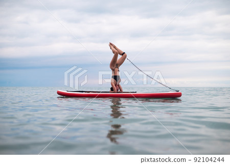 a sporty girl on a board in the sea stands on her head SUP yoga 92104244