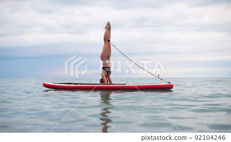 a sporty girl on a board in the sea stands on her head SUP yoga a sporty girl on a board in the sea stands on her head SUP yoga 92104246