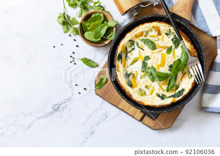 Spinach and cheese omelette. Frittata made of eggs, paprika and spinach in a frying pan on a marble countertop. View from above. Copy space. Spinach and cheese omelette. Frittata made of eggs, paprika and spinach in a frying pan on a marble countertop. View from above. Copy space. 92106036
