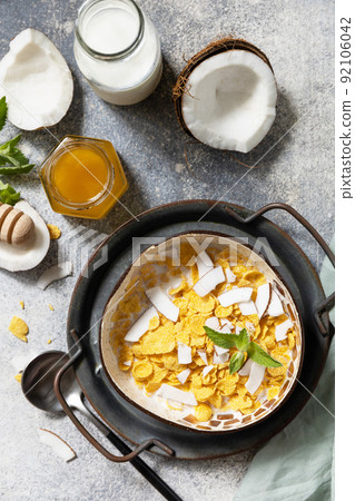 Vegan healthy breakfast. Cereal granola breakfast flakes with coconut non-dairy alternative milk and fresh coconut slices on a stone tabletop. View from above. 92106042