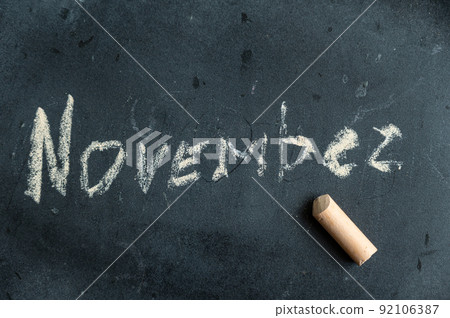 November. Name of autumn month written in yellow chalk on black chalk board. Handwritten text. A piece of colored chalk lies next to it. 92106387