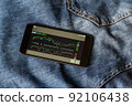 Stock market and cryptocurrency chart on your smartphone screen, which includes an up trend and a down trend. Stock market investment. The smartphone lies on top of the blue jeans. 92106438