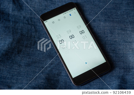 Black smartphone with the Time Countdown App open. Zeros on the screen of the device. The starting point of the countdown. Against the blue jeans. 92106439