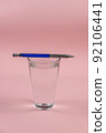 A glass of water and a pencil on a pink background. A full glass of drinking water. Blue and silver metallic pencil. Kurp plan. Selective focus. 92106441