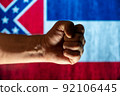Tightly clenched male fist in front of state Mississippi flag. Concept of independence, freedom, and unity. Selective focus. 92106445