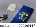Smartphone, door keys, and paper house on gray background. New York State flag on screen of your device. Buying or renting homes. Moving to live in New York State. Selective Focus. 92106447