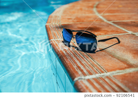 Sunglasses on side of pool with clear turquoise water. No people copy space Sunglasses on side of pool with clear turquoise water. No people copy space 92106541