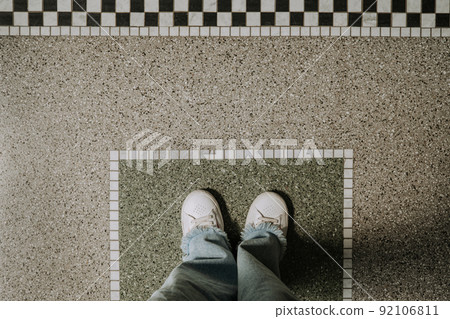 Top view of woman legs in jeans and white sneakers on pattern tile floor. Copy space, teenager 92106811