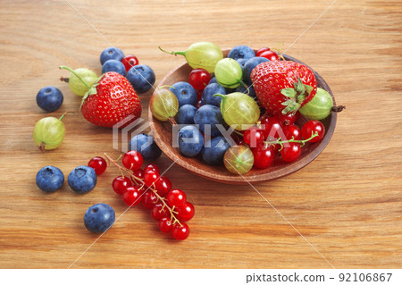 Berries mix in in a heart shaped bowl spilled on rustic wooden table 92106867