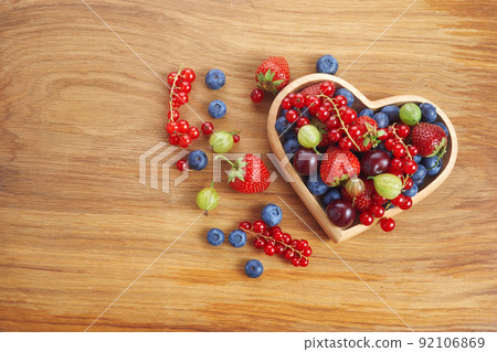 Berries mix in in a heart shaped bowl spilled on rustic wooden table 92106869
