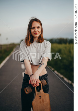 Vertical poster. portrait sexy teen girl with tattoo leaning on a longboard looks into the camera. 92107035