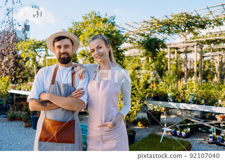 Owners of garden centre in aprons are looking to camera. Copyspace Owners of garden centre in aprons are looking to camera. Copyspace 92107040