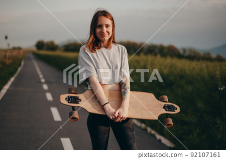 Funny teen girl in jeans and top stands with big skate. bike path in the background Funny teen girl in jeans and top stands with big skate. bike path in the background 92107161