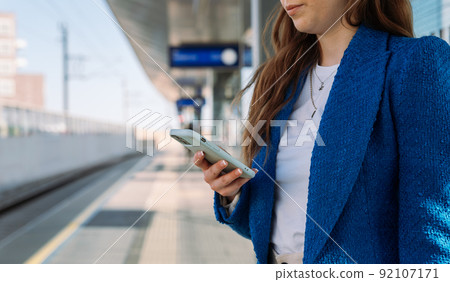 Midsection. Young stylish woman using mobile while waiting for train at station. Public transport. Midsection. Young stylish woman using mobile while waiting for train at station. Public transport. 92107171