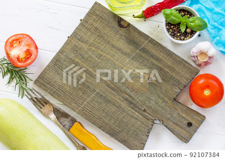 White wooden kitchen background. Cutting board and fresh vegetables, olive oil and spices on the kitchen table, copy space, top view. 92107384