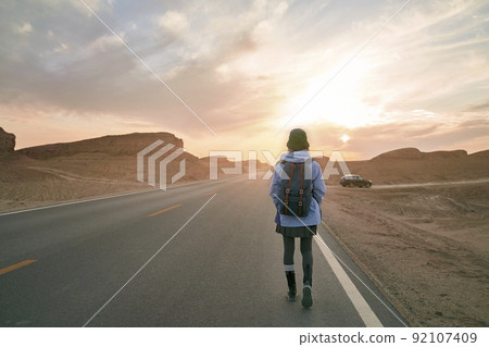 rear view of woman traveler walking on highway in gobi desert with yardang landforms rear view of woman traveler walking on highway in gobi desert with yardang landforms 92107409