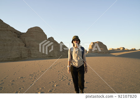 asian woman traveler backpacker walking in desert at sunset with yardang landform in background 92107820