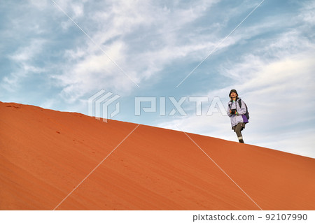 asian woman photographer walking on the ridge of a sand dune looking at view asian woman photographer walking on the ridge of a sand dune looking at view 92107990