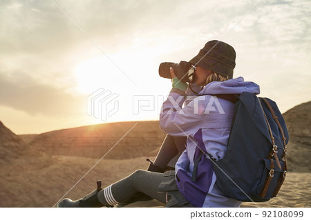 asian woman female photographer taking a photo of landscape in gobi desert with yardang landforms at sunset asian woman female photographer taking a photo of landscape in gobi desert with yardang landforms at sunset 92108099