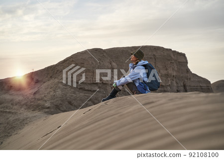 young asian woman backpacker sitting on ground relaxing resting watching sunset 92108100