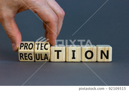 Protection and regulation symbol. Businessman turns cubes changes the word regulation to protection. Beautiful grey table, grey background, copy space. Business, protection and regulation concept. 92109315