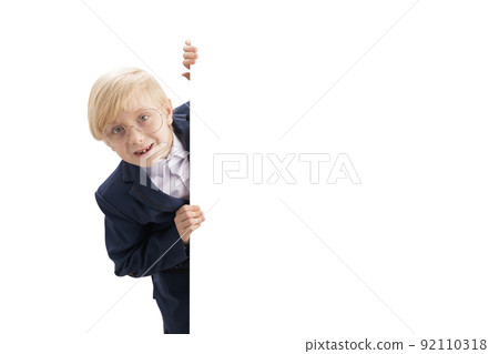 Cheerful blond boy in big glasses and school uniform peeking from behind white backdrop. Copy space. Studio shot. Isolate Cheerful blond boy in big glasses and school uniform peeking from behind white backdrop. Copy space. Studio shot. Isolate 92110318