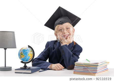 Cheerful boy first grader in students hat and large glasses next to notebooks and globe. Studying and education concept. Cheerful boy first grader in students hat and large glasses next to notebooks and globe. Studying and education concept. 92110319