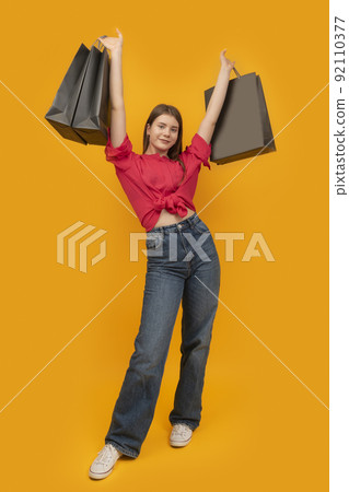 Stylish happy young woman holds several paper bags after shopping. Yellow background. Black Friday Concept. Vertical frame. Stylish happy young woman holds several paper bags after shopping. Yellow background. Black Friday Concept. Vertical frame. 92110377