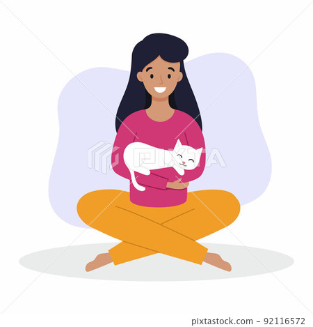 A girl holds a cat in her arms. A woman with a cat is sitting on the floor. Owner and pet. A girl holds a cat in her arms. A woman with a cat is sitting on the floor. Owner and pet. 92116572