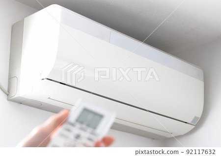 White air conditioner and hands to operate the remote control 92117632