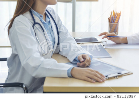 Two asian women doctors discuss meeting doctor's office medical clinic looking x-ray film consulting patient disease. Asian medical lab young women talking together discussing healthcare teamwork Two asian women doctors discuss meeting doctor's office medical clinic looking x-ray film consulting patient disease. Asian medical lab young women talking together discussing healthcare teamwork 92118087