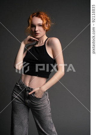 Confident young woman standing in gray studio with hand on waist 92118835