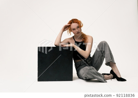 Confident young lady sitting on ground and looking at camera 92118836