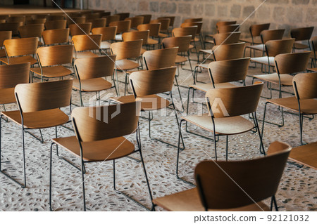 Set of empty wooden chairs lined up before an event in an ancient church or castle with medieval floor and walls. Selective focus. 92121032