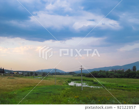 Power line poles in a summer grassy field and beautiful clouds above them 92122857