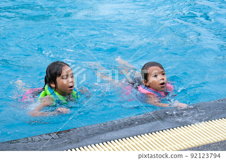 Happy little sisters play in outdoor swimming pool of tropical resort during family summer vacation. Kids learning to swim. Healthy Summer Activities for Kids. Happy little sisters play in outdoor swimming pool of tropical resort during family summer vacation. Kids learning to swim. Healthy Summer Activities for Kids. 92123794