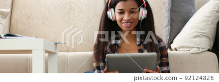 Latin young woman sit on carpet with tablet and watch show, lady in headset 92124828