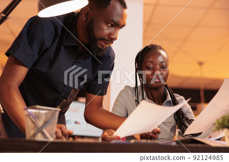 Office colleagues working together as business team to create project report with research information and data charts on paperwork. Doing teamwork and analyzing presentation ideas on files. Office colleagues working together as business team to create project report with research information and data charts on paperwork. Doing teamwork and analyzing presentation ideas on files. 92124985