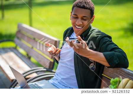 Smiling man talking holding smartphone at mouth level Smiling man talking holding smartphone at mouth level 92126332